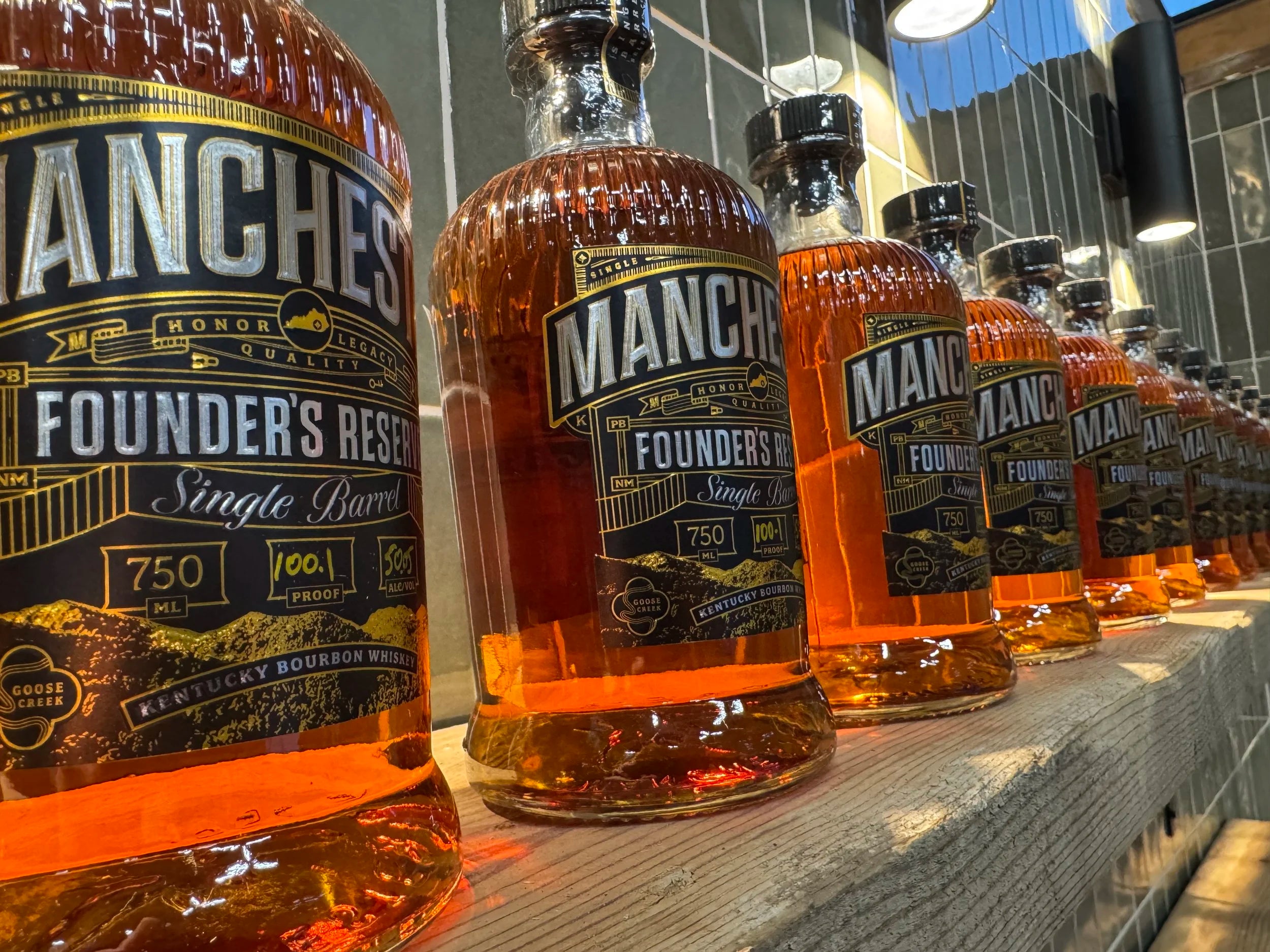 Bottles of Manchester Founder's Reserve bourbon lined up on a bar counter.